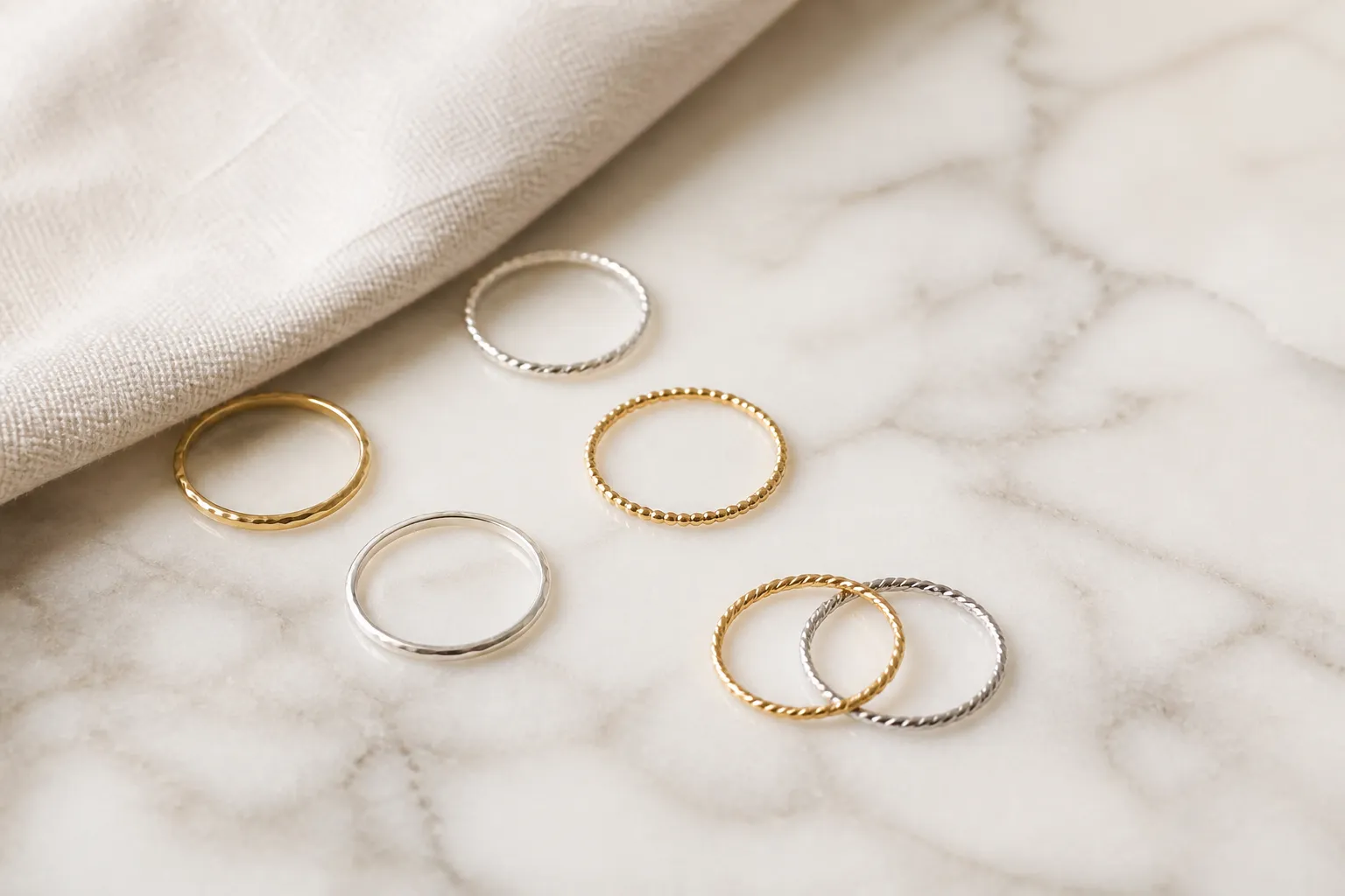 Delicate gold and silver rings arranged on a light marble surface